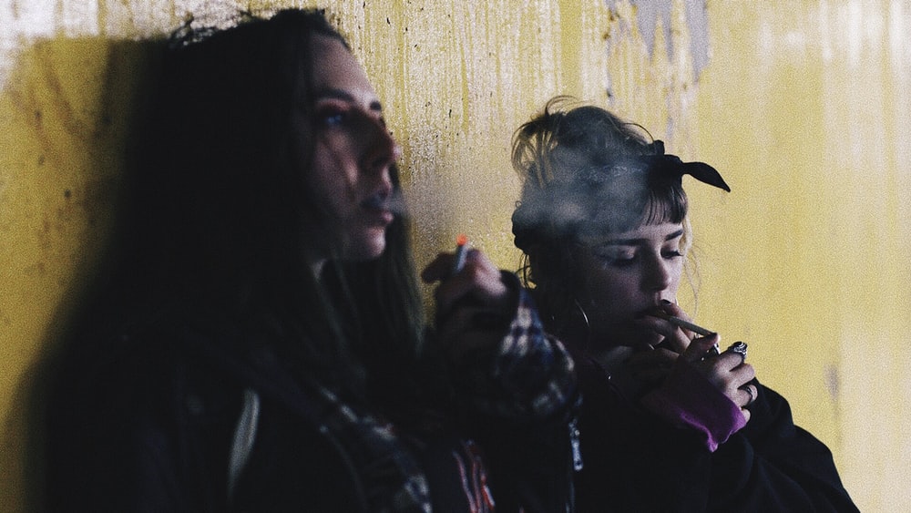 4 Unpleasant Effects Of Drugs On Physical Health Two Women Smoking While Leaning On Yellow Wall